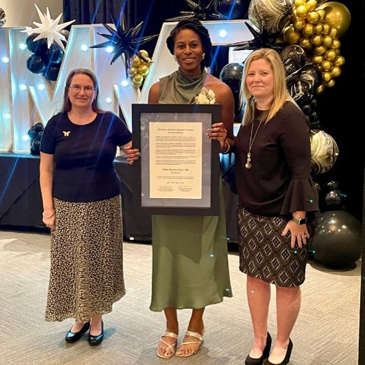 Nneka Agum stands with two faculty members holding an award.